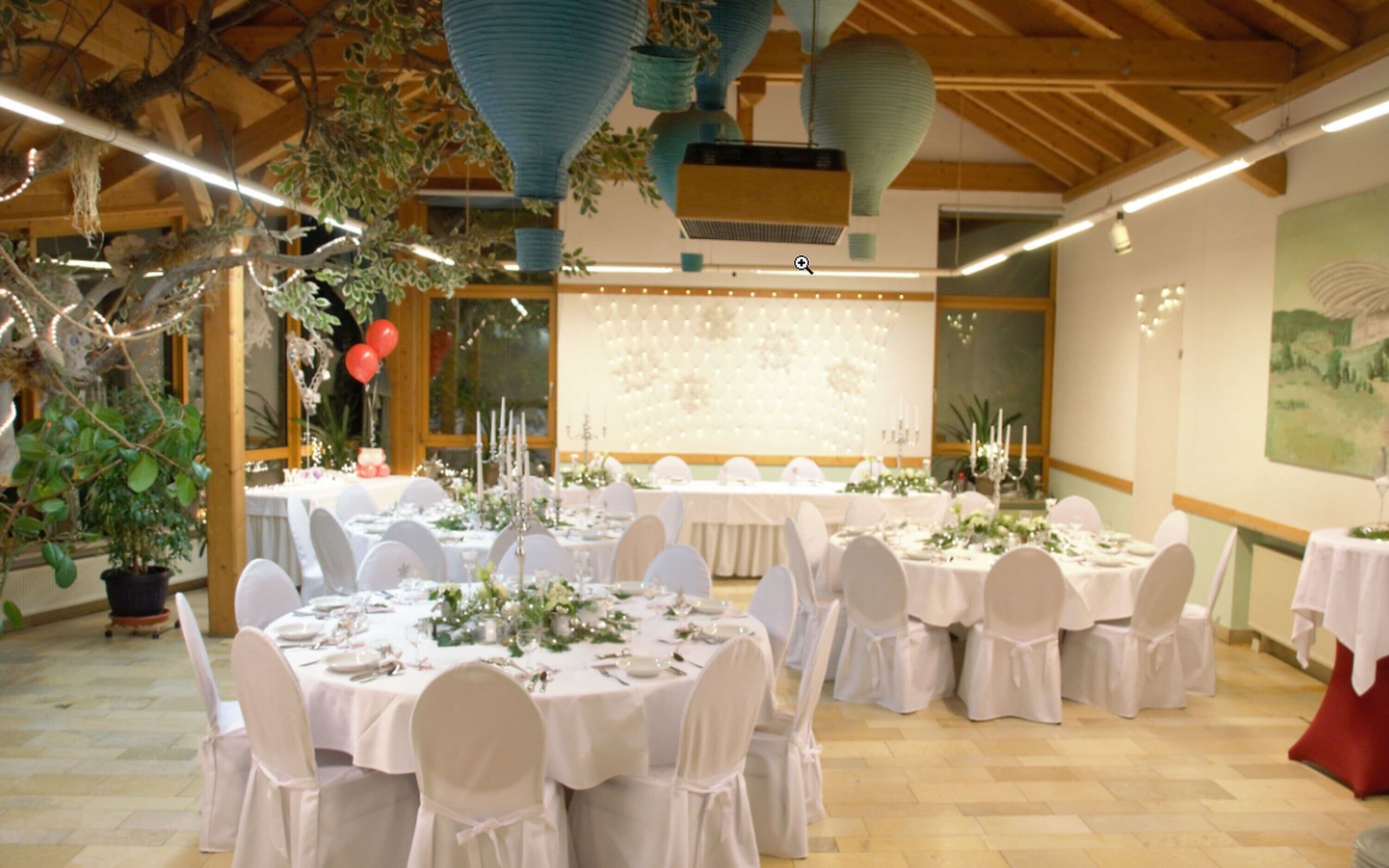 A banquet hall with round tables set for a formal event, featuring white tablecloths and chairs, and a large floral backdrop.