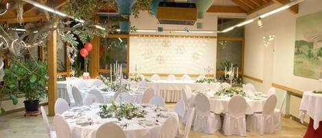 A banquet hall with round tables set for a formal event, featuring white tablecloths and chairs, and a large floral backdrop.