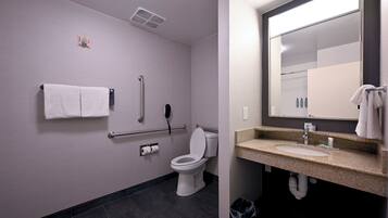A modern bathroom with a toilet, handrails, a towel rack, a sink, and a mirror.