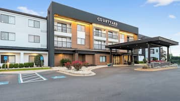 Ein Courtyard by Marriott Hotel mit überdachter Zufahrt, Parkplatz und einer begrünten Anlage mit Sträuchern und Blumen.