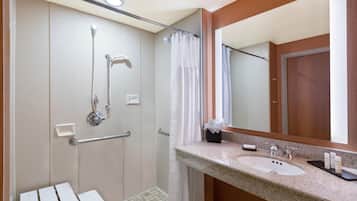 A bathroom with a shower, grab bars, a sink, and a mirror.