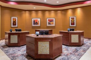 A reception area with three counters, each equipped with a computer and a phone. The walls are adorned with framed artwork. - Embassy Suites by Hilton St. Louis St. Charles (St. Charles)