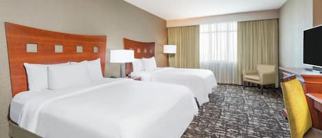 A hotel room with two beds, a desk with a chair, a television, and a window with curtains.