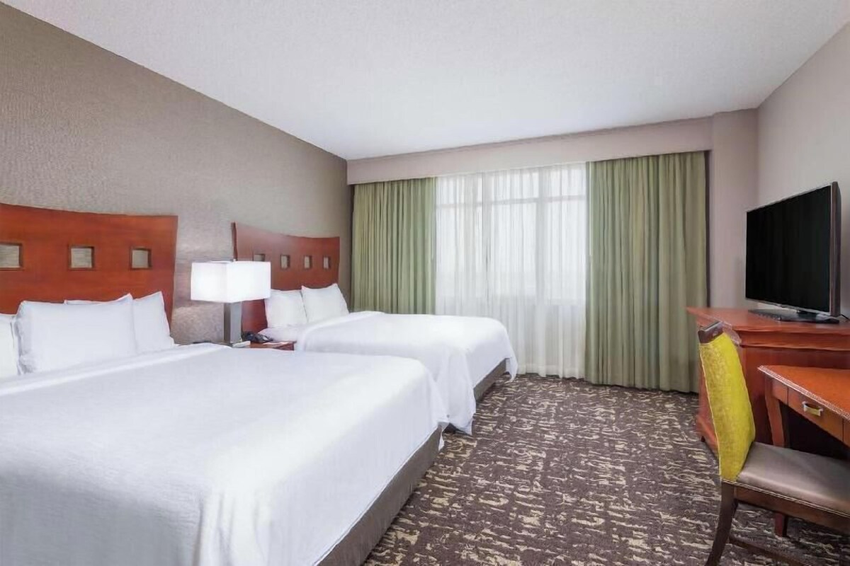 A hotel room with two beds, a desk with a television, and a chair.