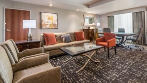 A hotel room with a sofa, armchairs, a coffee table, a desk, and a large window with curtains. - Embassy Suites by Hilton St. Louis St. Charles (St. Charles)