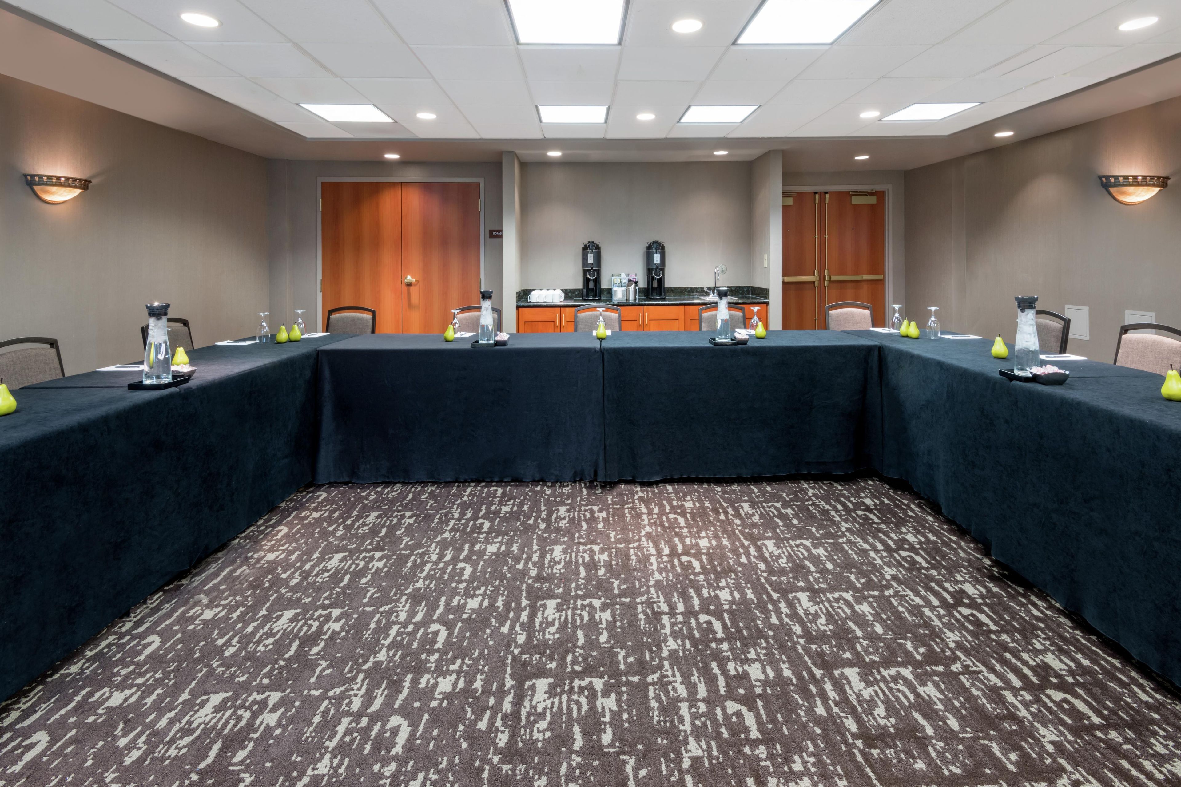 A conference room with a long table, chairs, a kitchenette, and a door.