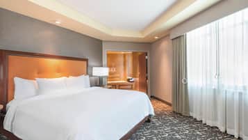 A hotel room with a large bed, a desk, a chair, and a bathroom visible through an open door.