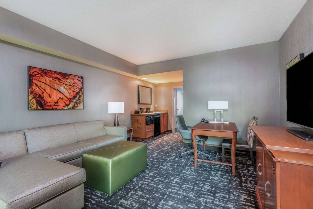 Habitación de hotel con sofá, reposapiés, escritorio, silla, televisor y lámpara de escritorio.