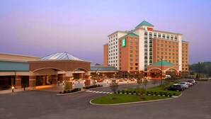 A multi-story hotel with a central courtyard, a parking lot, and a green-roofed building. - Embassy Suites by Hilton St. Louis St. Charles (St. Charles)