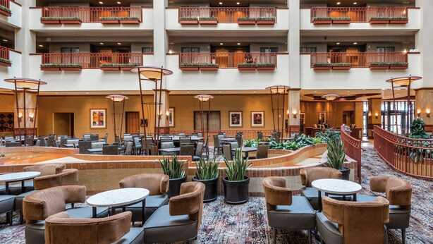 A spacious indoor lobby with multiple seating areas, including round tables and sofas, and a central water feature. - Embassy Suites by Hilton St. Louis St. Charles (St. Charles)