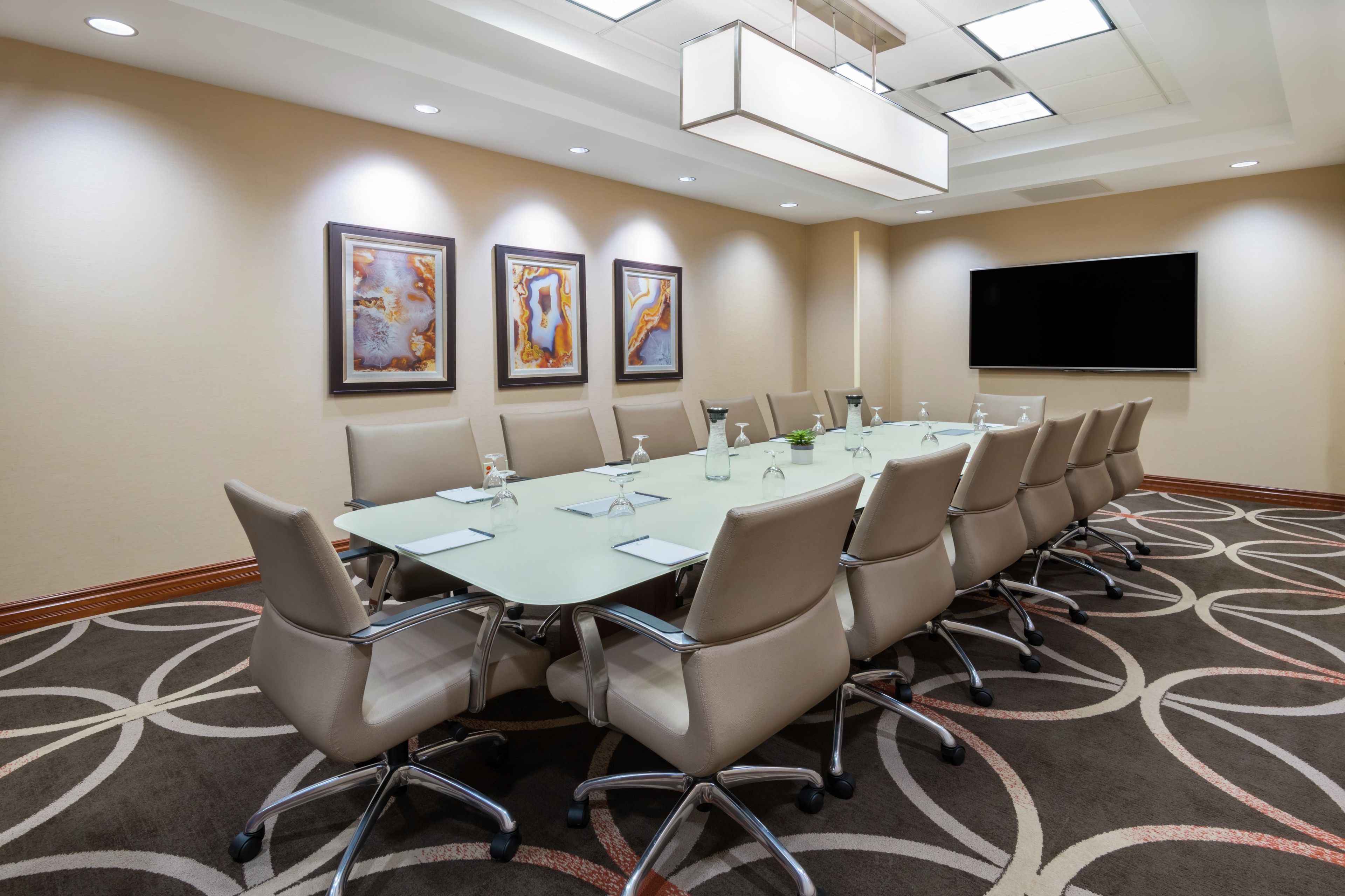 Un salón de conferencias con una larga mesa, varias sillas y un televisor de pantalla plana en la pared.