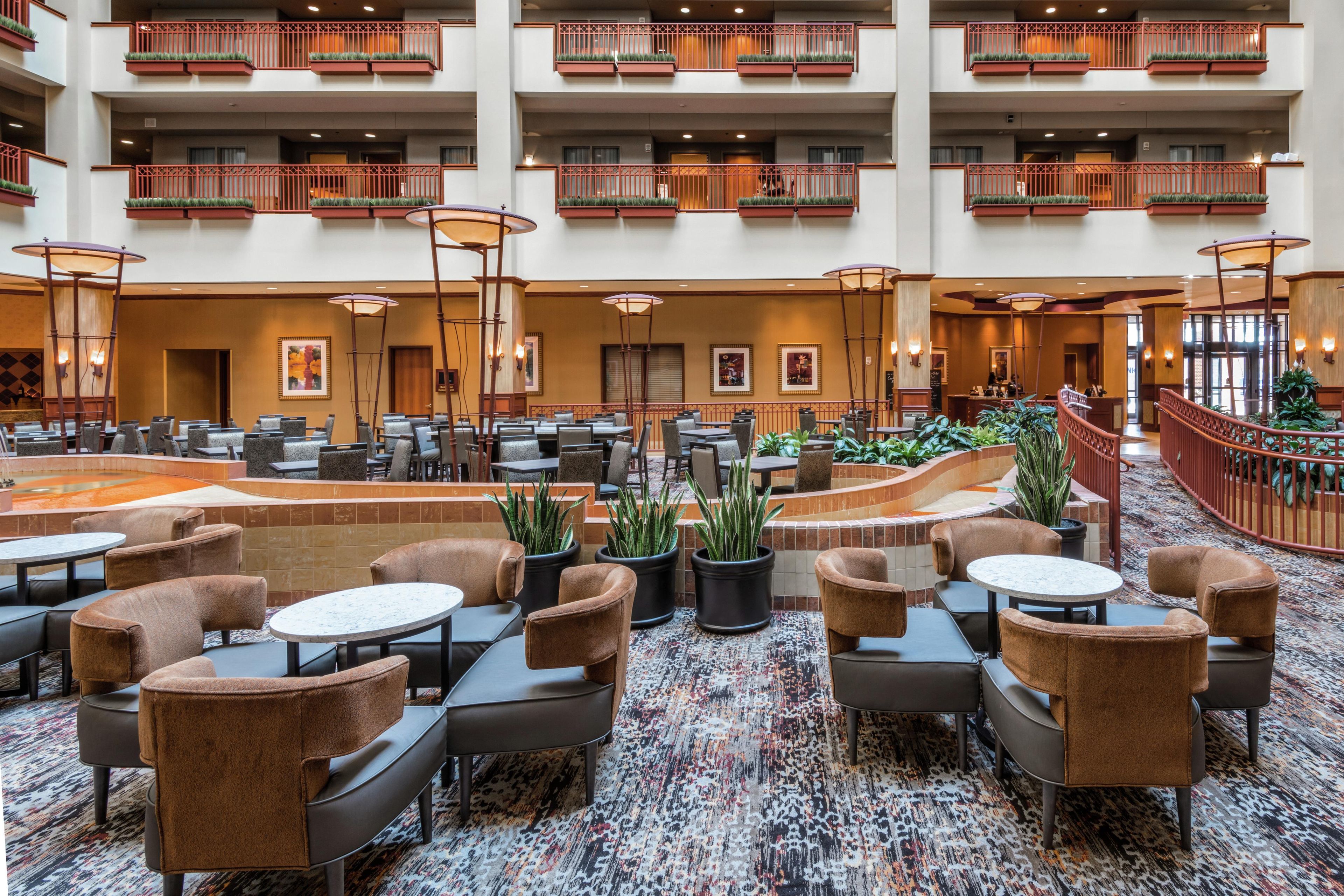 A multi-level hotel lobby with numerous seating areas, a central water feature, and a variety of plants.