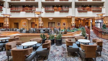 A multi-level hotel lobby with numerous seating areas, a central water feature, and a variety of plants.