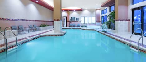 An indoor swimming pool with a 5-foot depth marker, seating areas, and a tiled border.