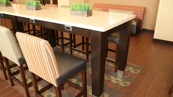 Un espace repas avec une longue table, des tabourets de bar et des carreaux de sol à motifs.