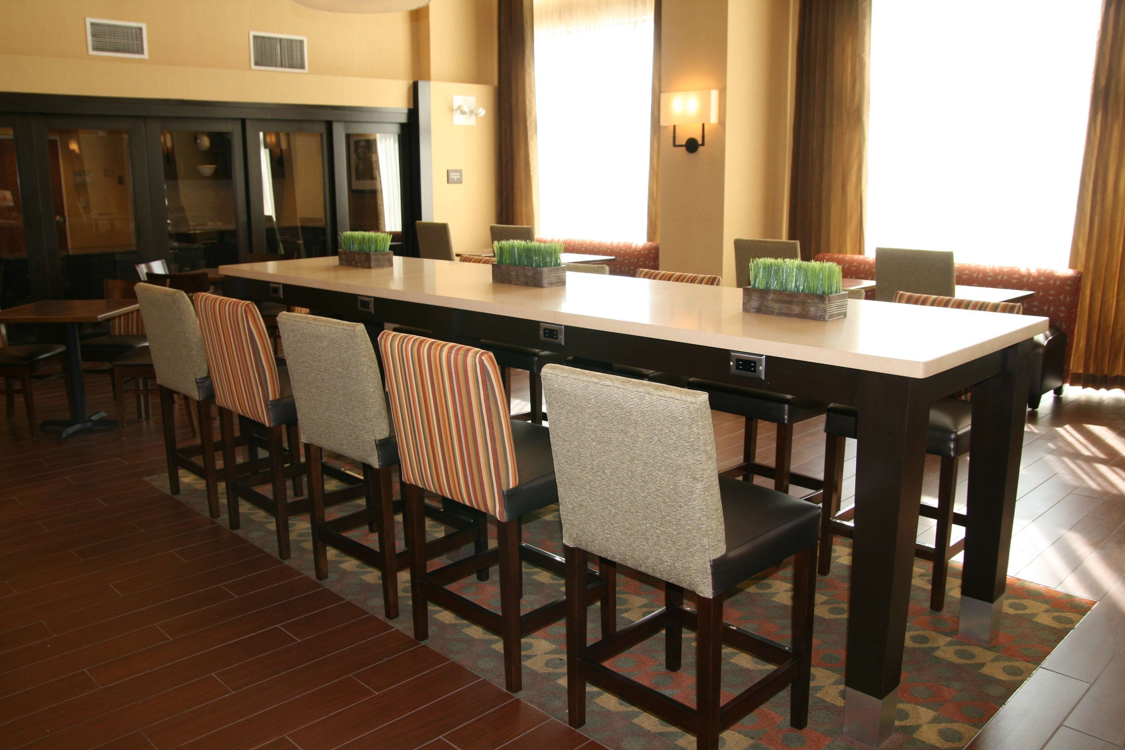 A hotel dining area with a long table, six chairs, and a small plant centerpiece.