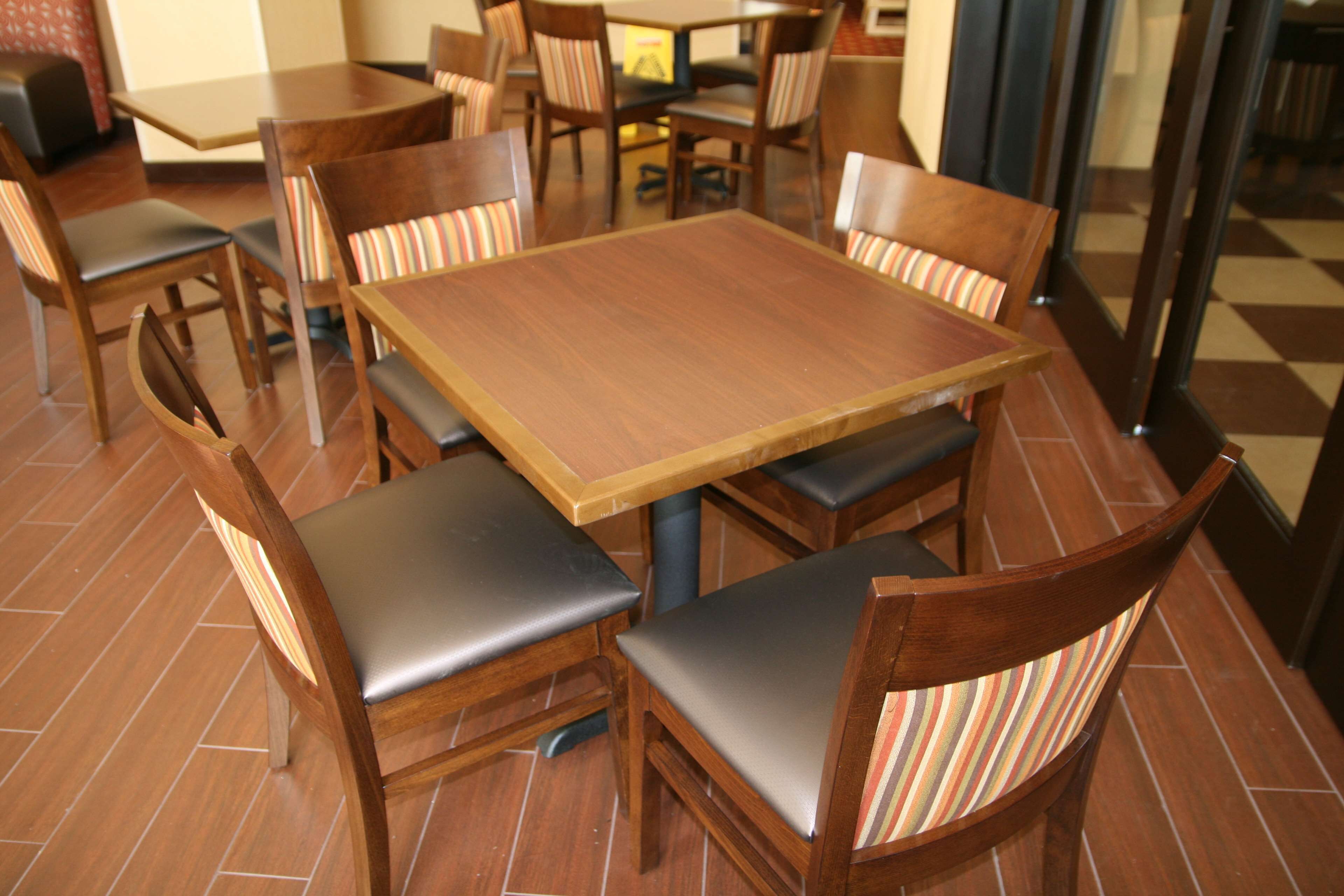 A dining area with wooden tables and chairs, some with striped cushions.