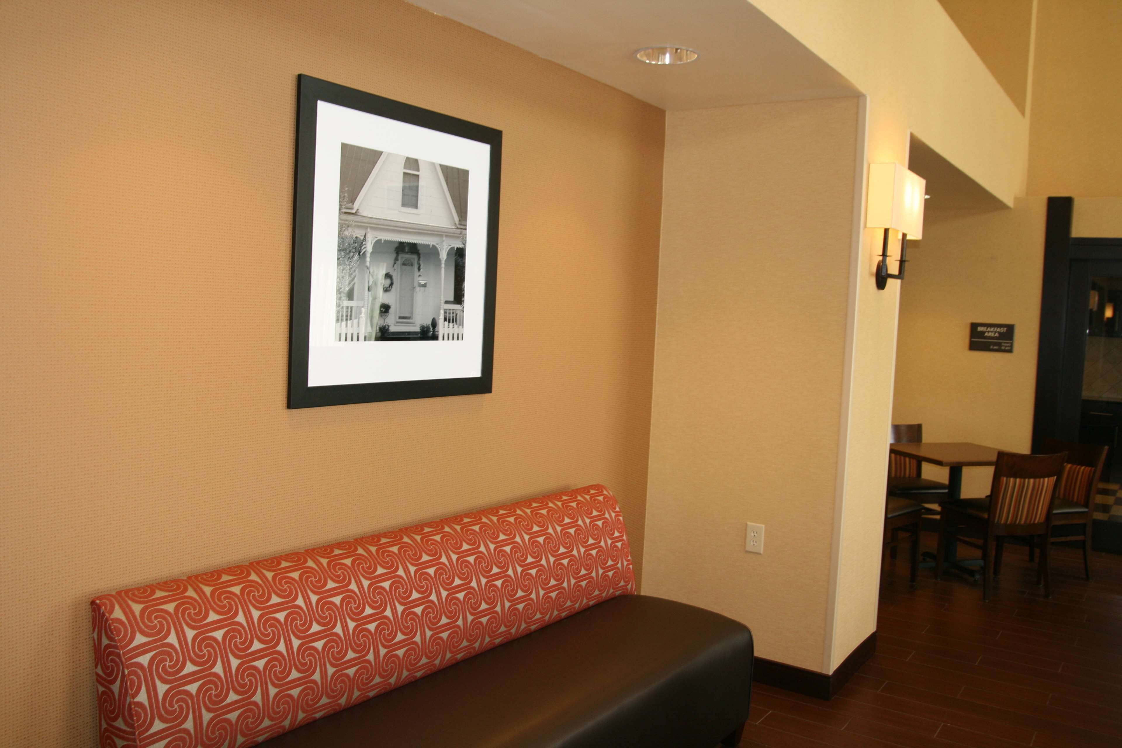 A hotel lobby with a bench, a framed picture on the wall, and a dining area in the background.