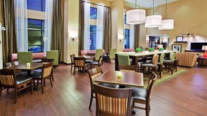 A hotel lobby with multiple seating areas, including tables and chairs, and a large TV screen. - Hampton Inn & Suites Oxford Anniston (Oxford)