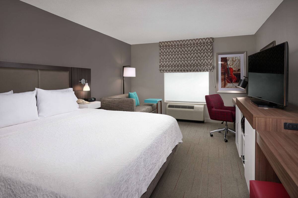 Habitación de hotel con una cama grande, un escritorio con una computadora, un televisor y una ventana con cortina estampada.