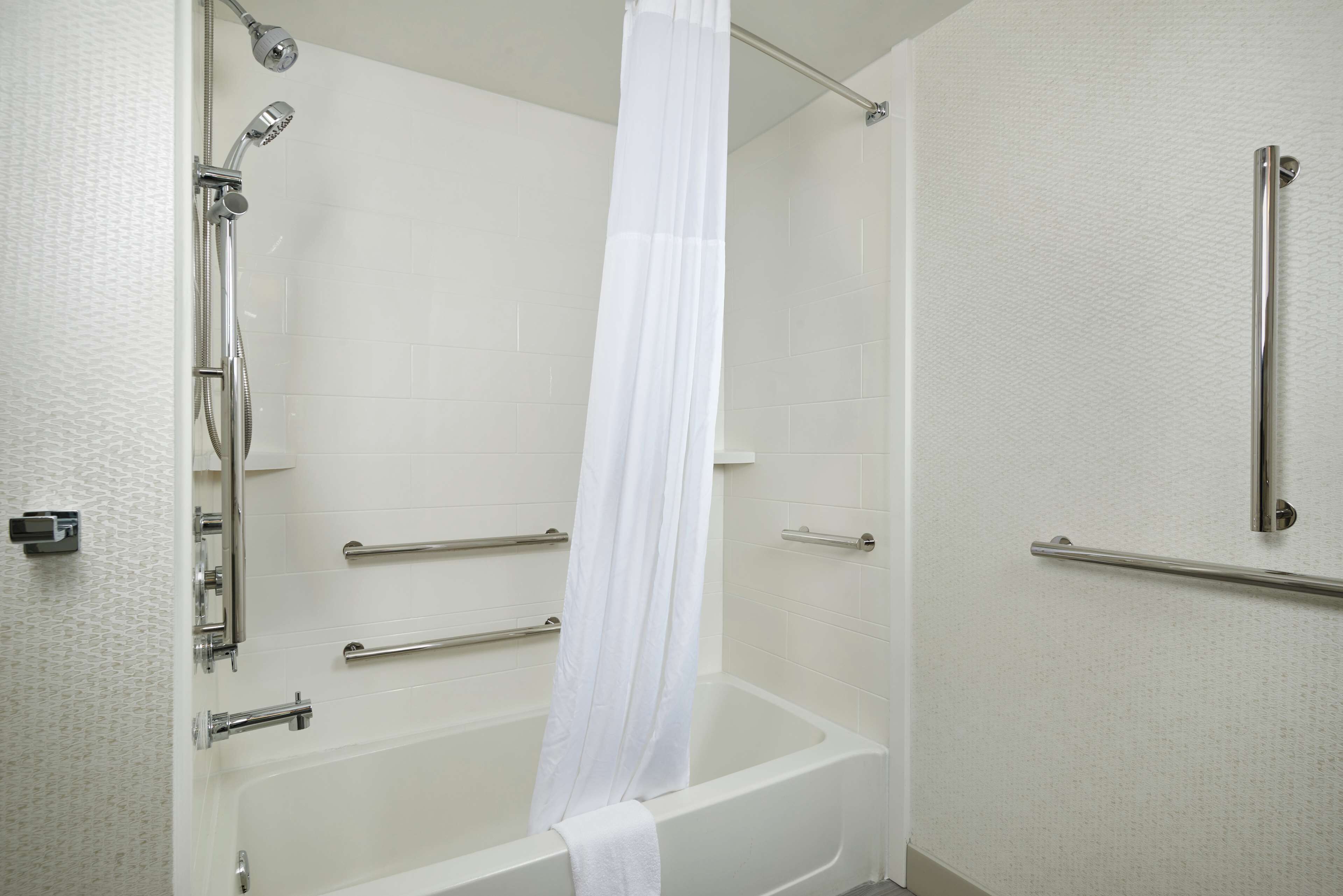 Un baño con bañera, ducha con cortina y barras de apoyo en las paredes.