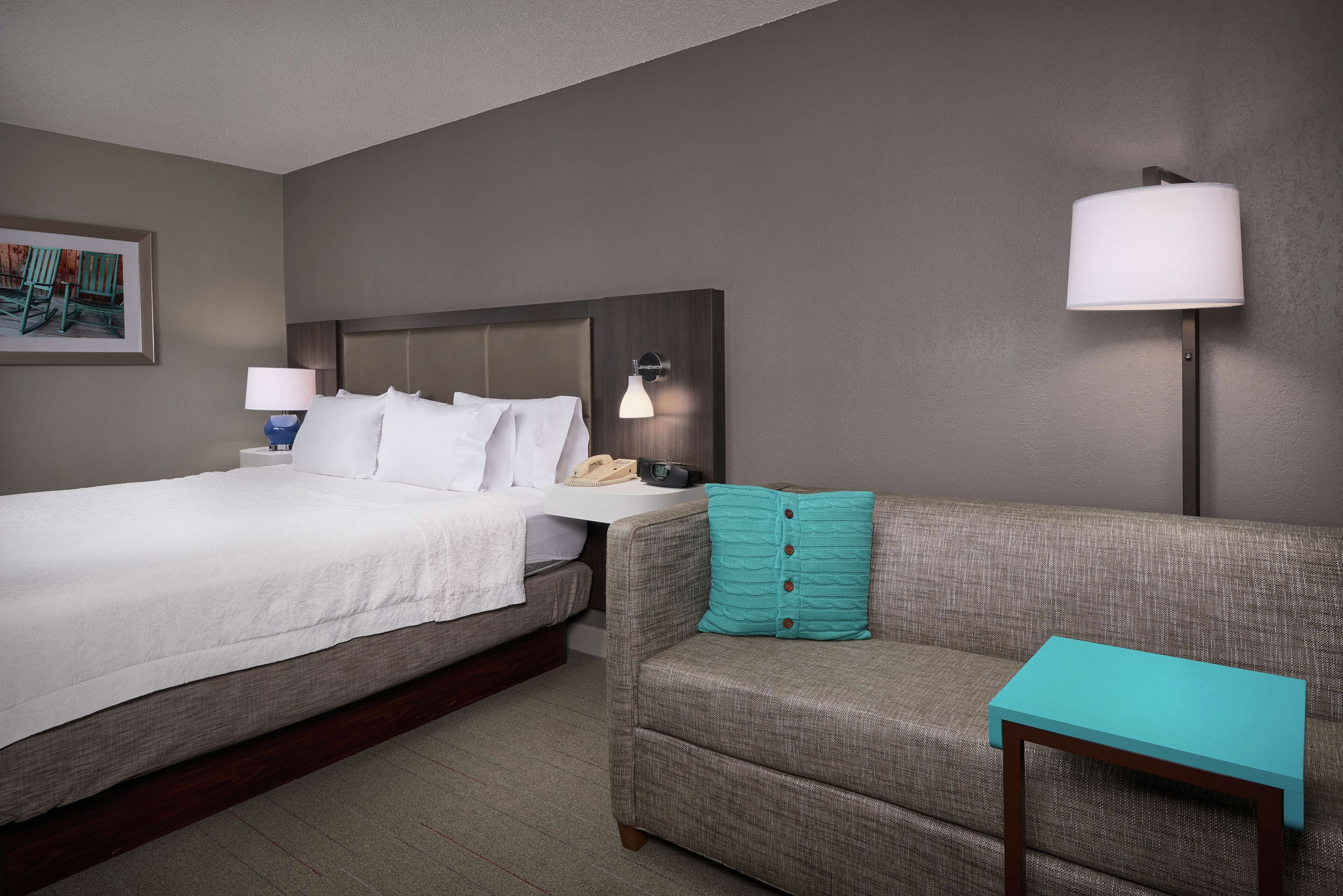 A hotel room with a bed, a sofa, a small table, a lamp, and a framed picture on the wall.