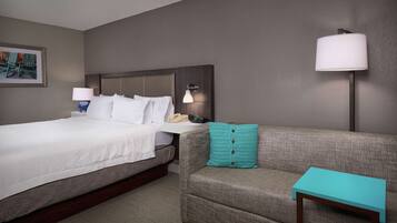 A hotel room with a bed, a sofa, a small table, a lamp, and a framed picture on the wall.