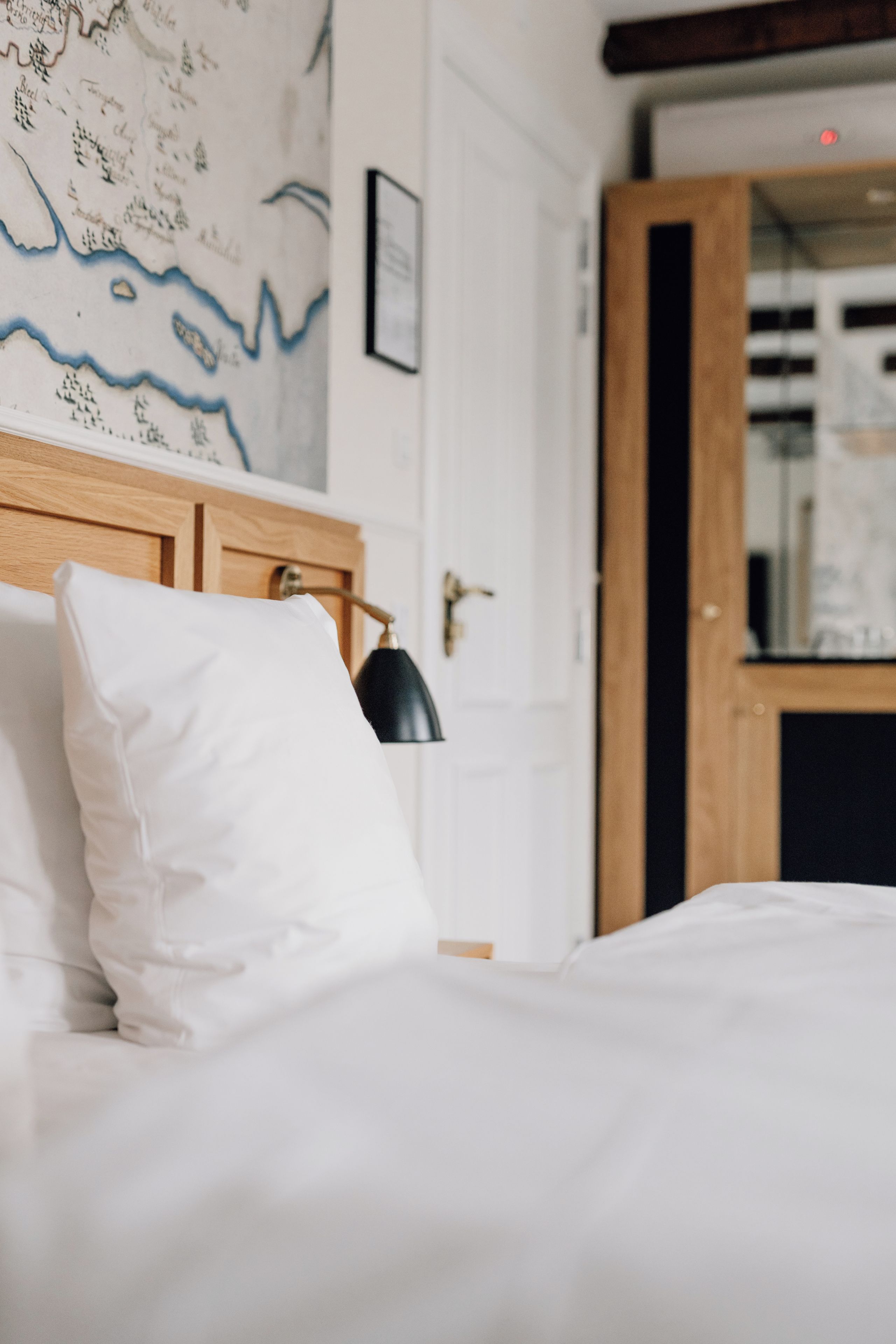 A bed with white bedding and a black lamp, a wooden headboard, and a wall with a map.