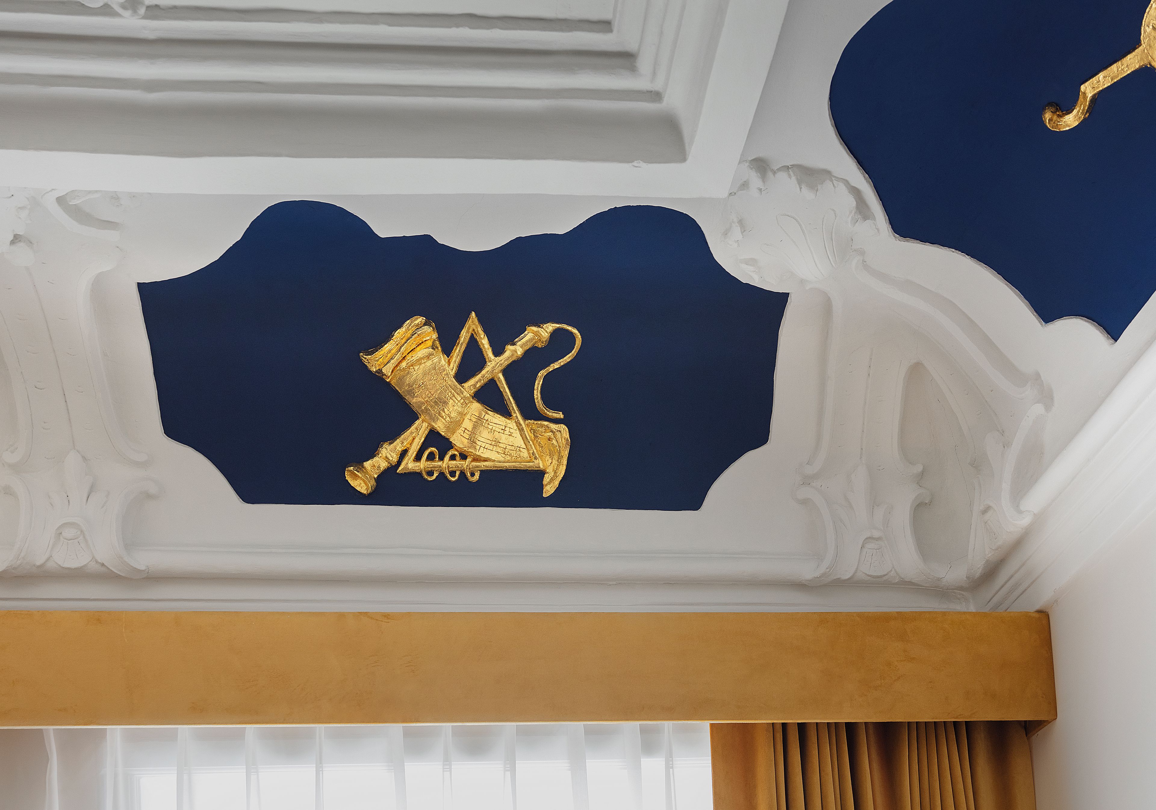 A ceiling with ornate white moldings and a gold emblem.