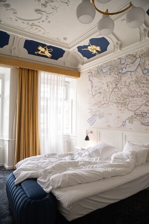 A bedroom with a large bed, a map on the wall, and a window with curtains.