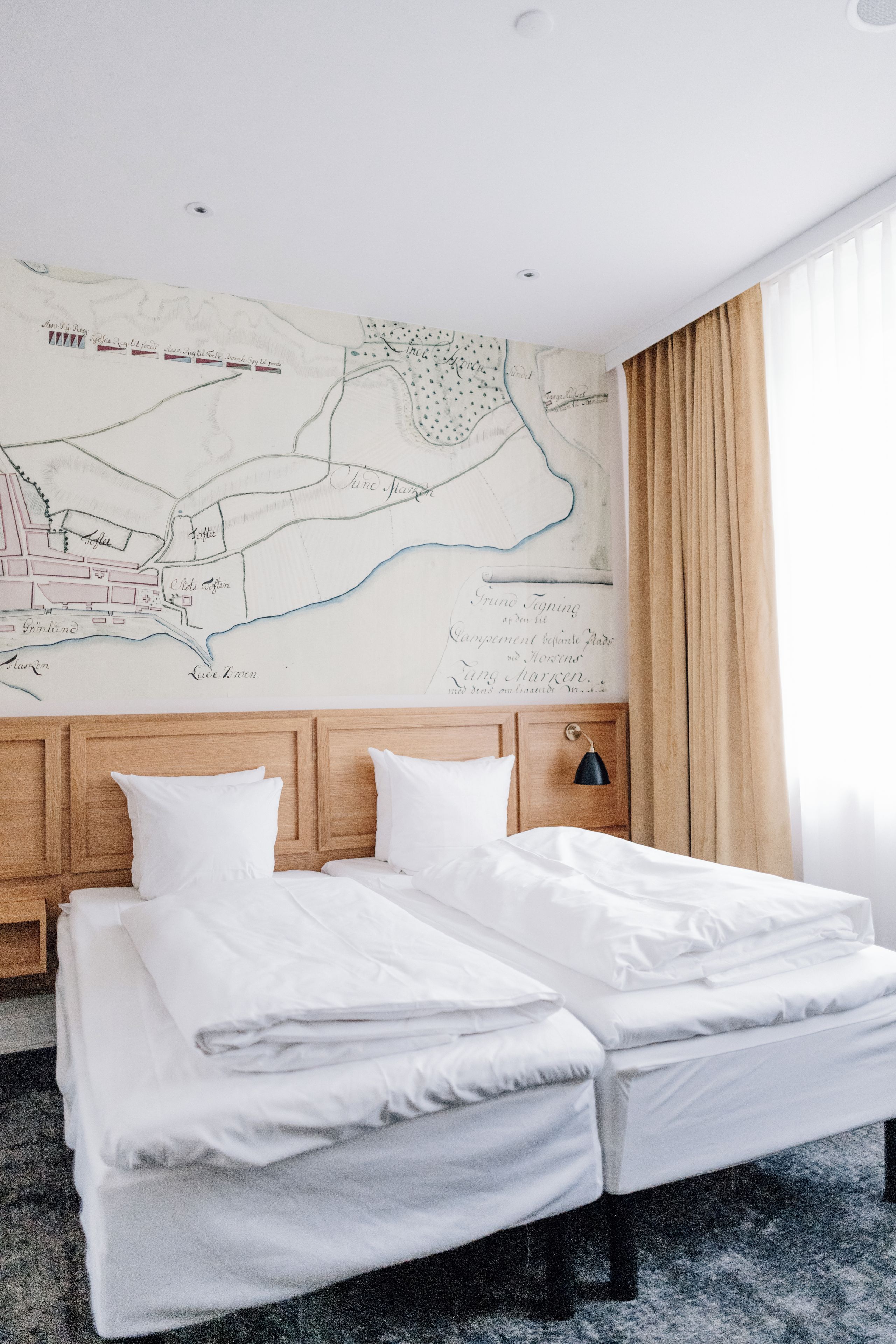 Habitación de hotel con una cama grande, cabecera de madera, un mapa en la pared y una ventana con cortinas.