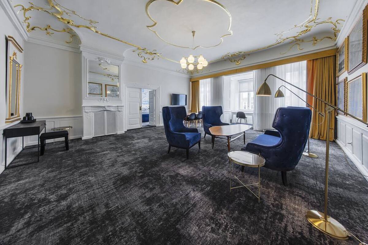 Une pièce avec une moquette sombre, des fauteuils bleus, une table ronde et un lampadaire doré.