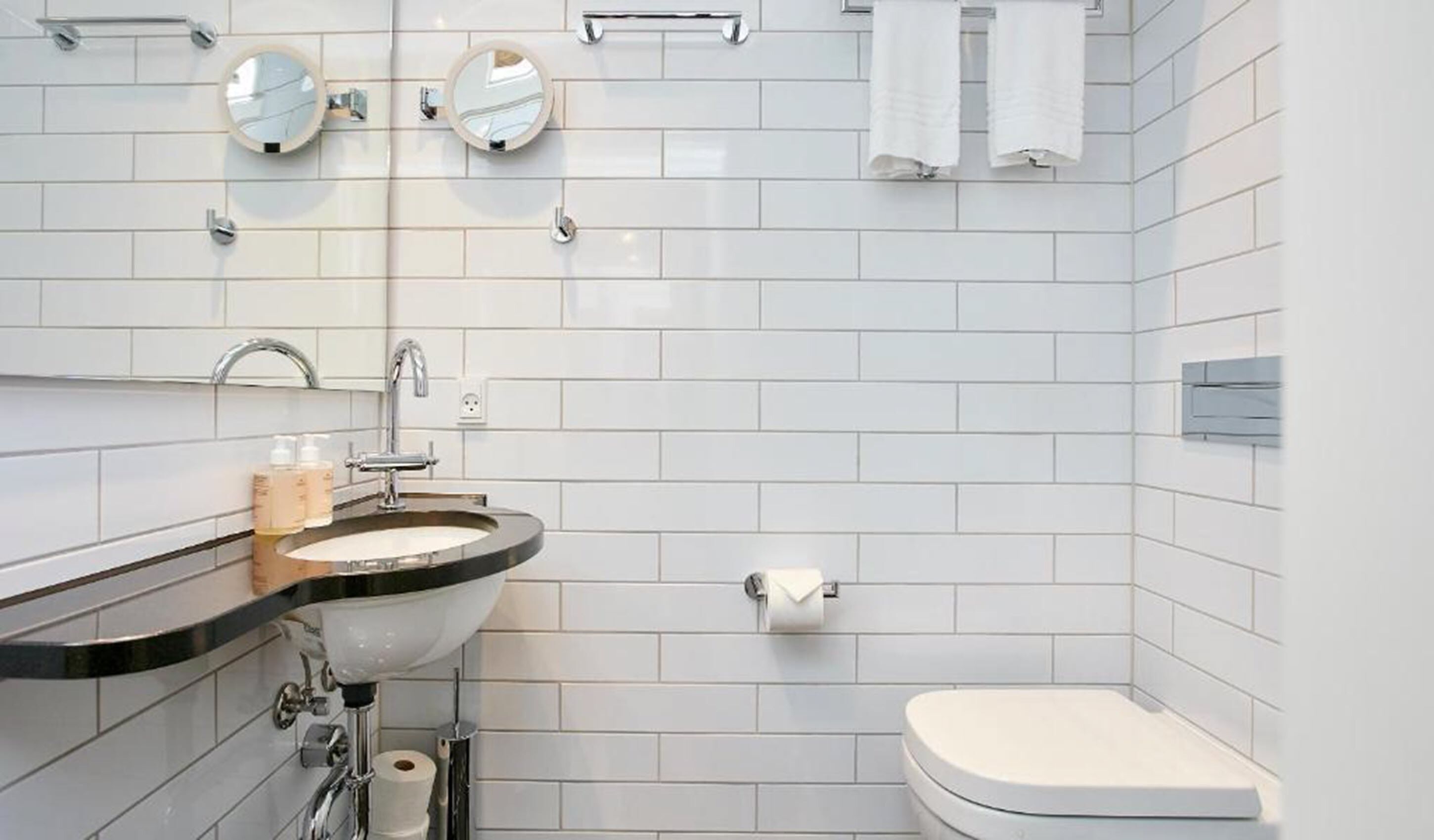 Un baño moderno con lavamanos, dos espejos, inodoro y toallero.