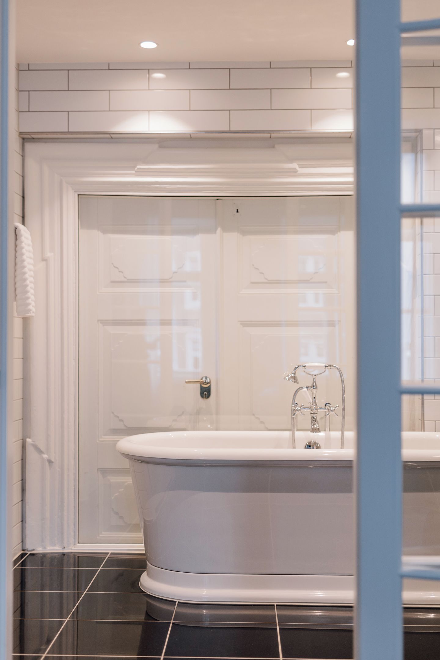 A bathroom with a white bathtub, a white door, and black tiled flooring.