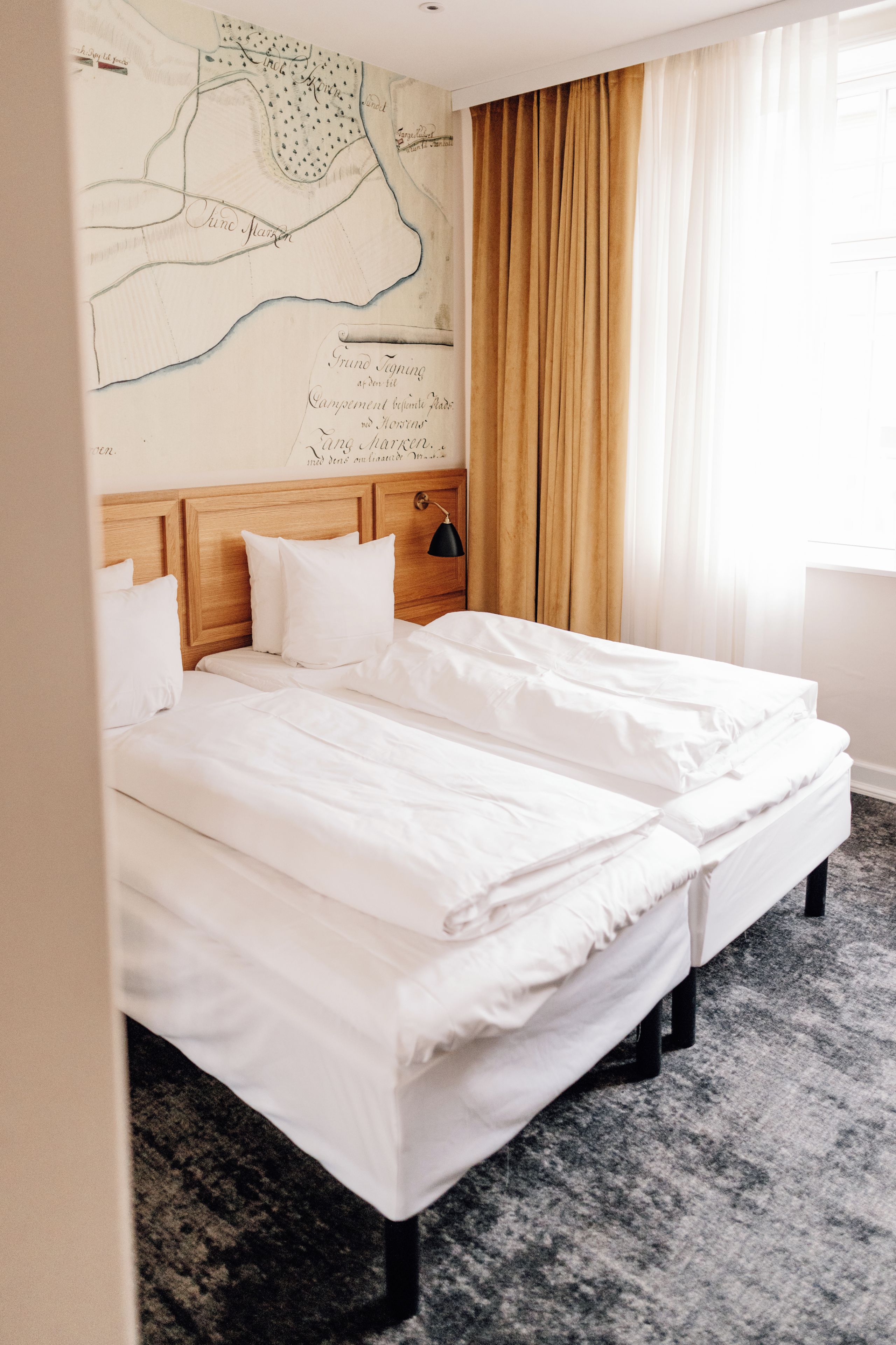Une chambre d’hôtel avec un grand lit, une tête de lit ornée d’une carte et une fenêtre avec des rideaux.