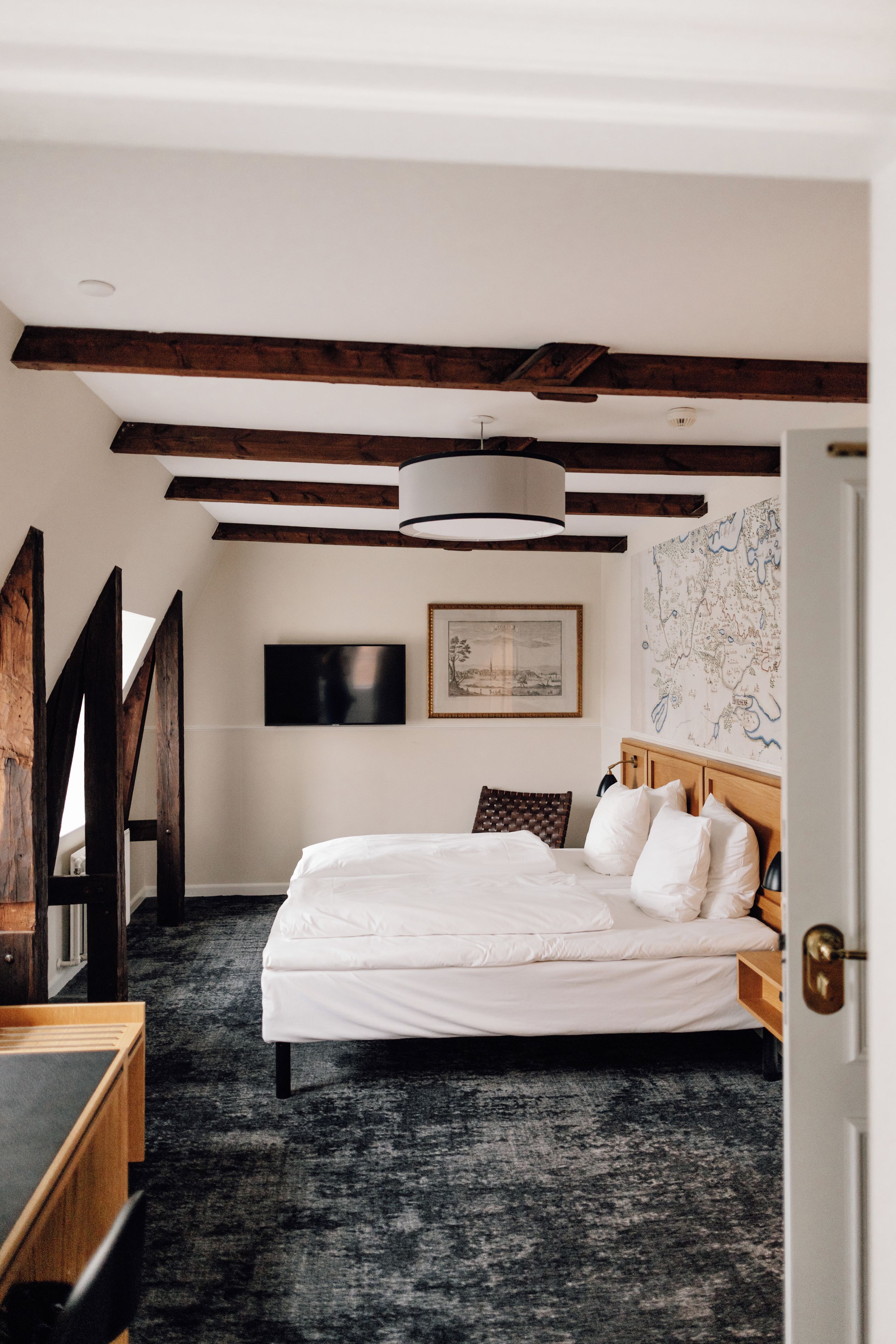 A bedroom with a large bed, a flat-screen TV, a map on the wall, and exposed wooden beams.