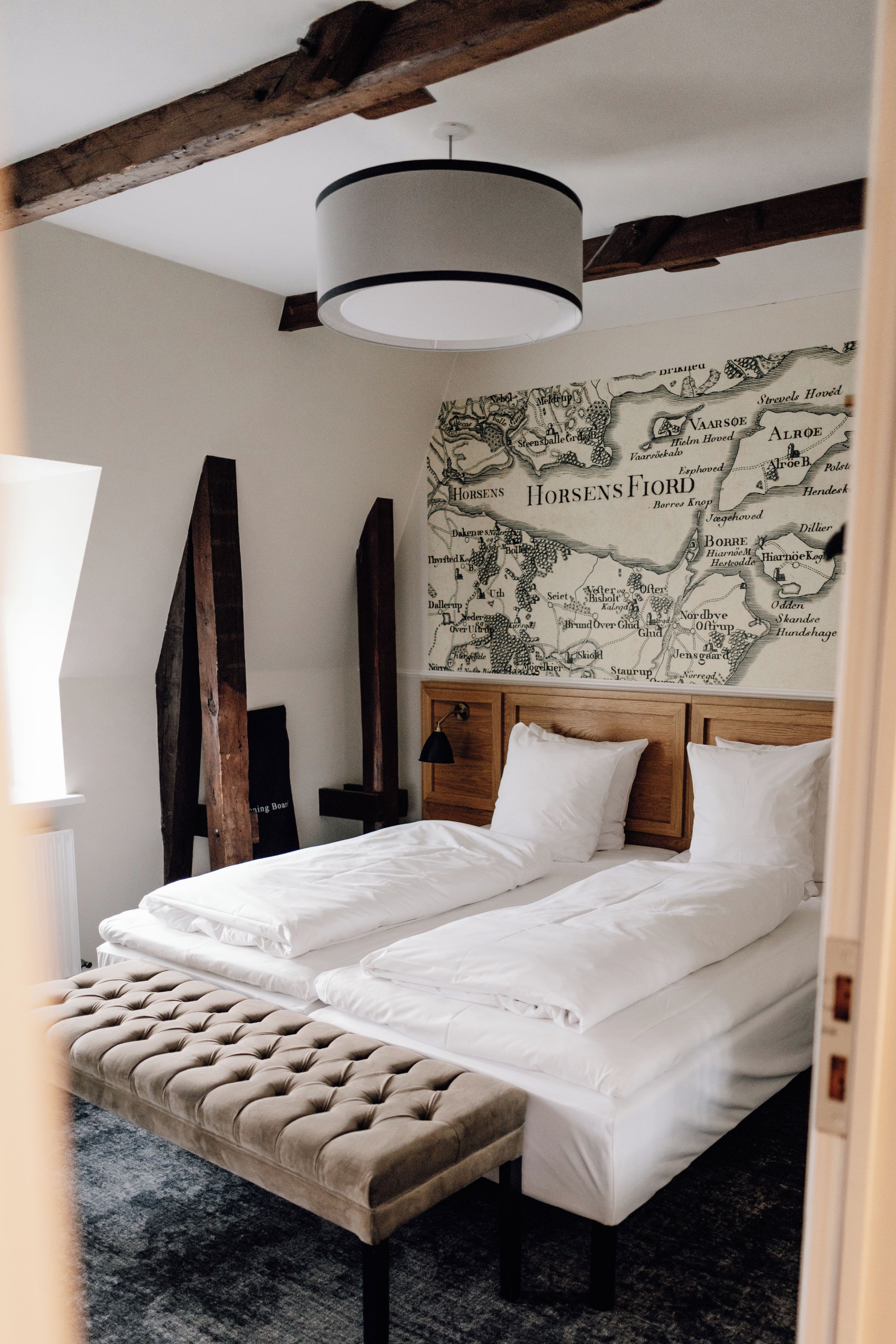Una cama doble con sábanas blancas, un cabecero de madera y un mural con un mapa en la pared.