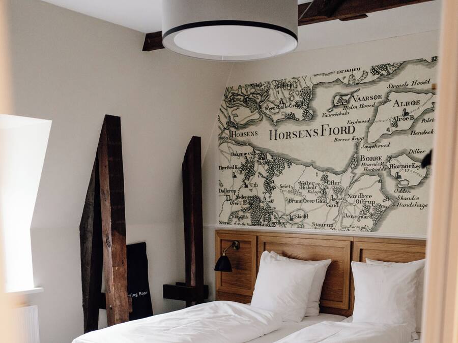 Una cama doble con sábanas blancas, un cabecero de madera y un mural con un mapa en la pared.
