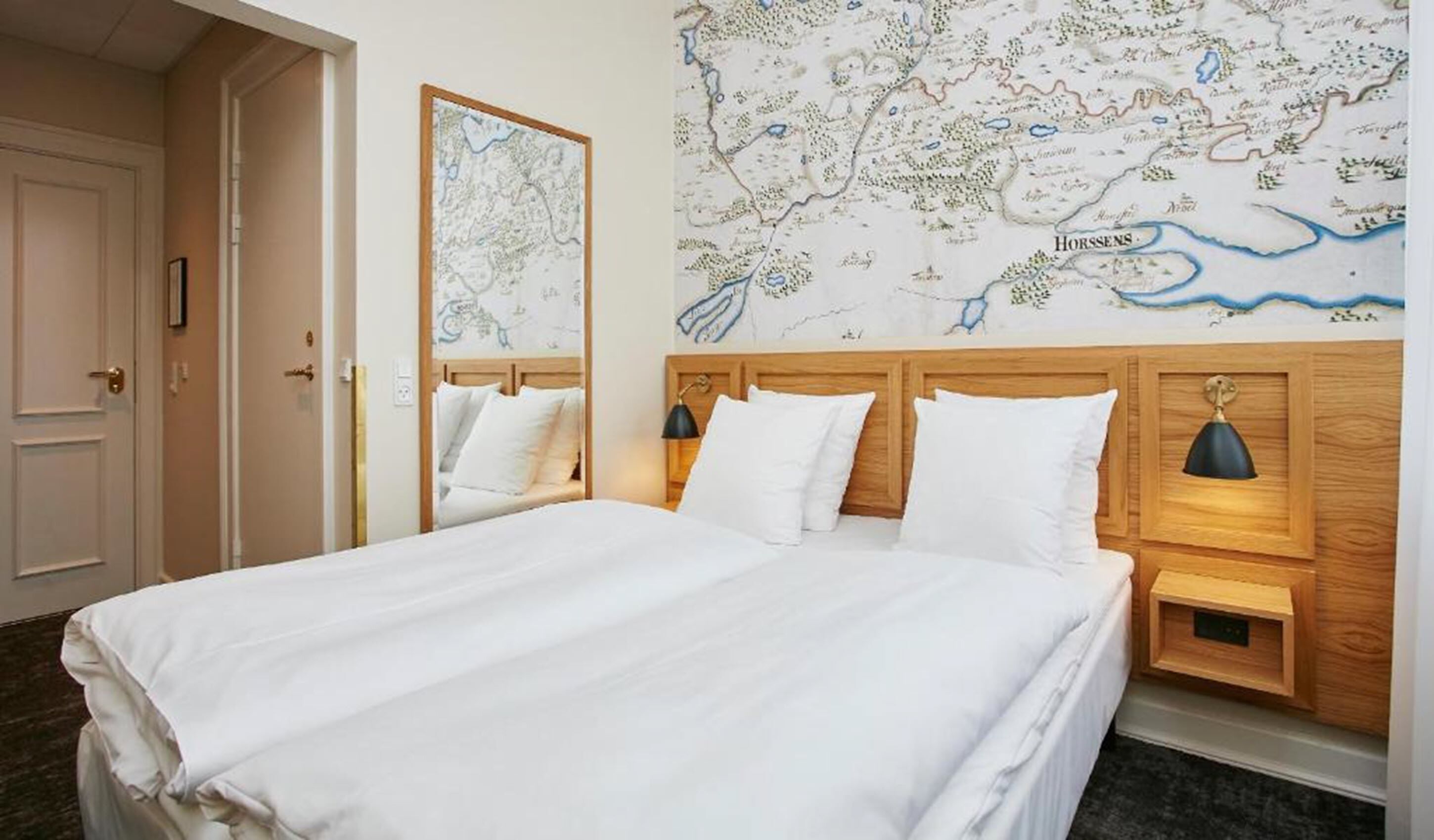 Ett hotellrum med en stor säng, två sängbord med lampor, en träpanel vid sänggaveln och en karta på väggen.