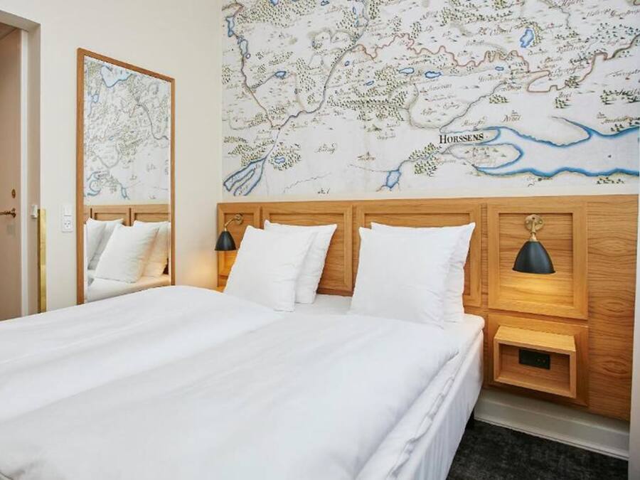 Habitación de hotel con una cama grande, dos mesitas de noche con lámparas, un cabecero de madera y un mapa en la pared.