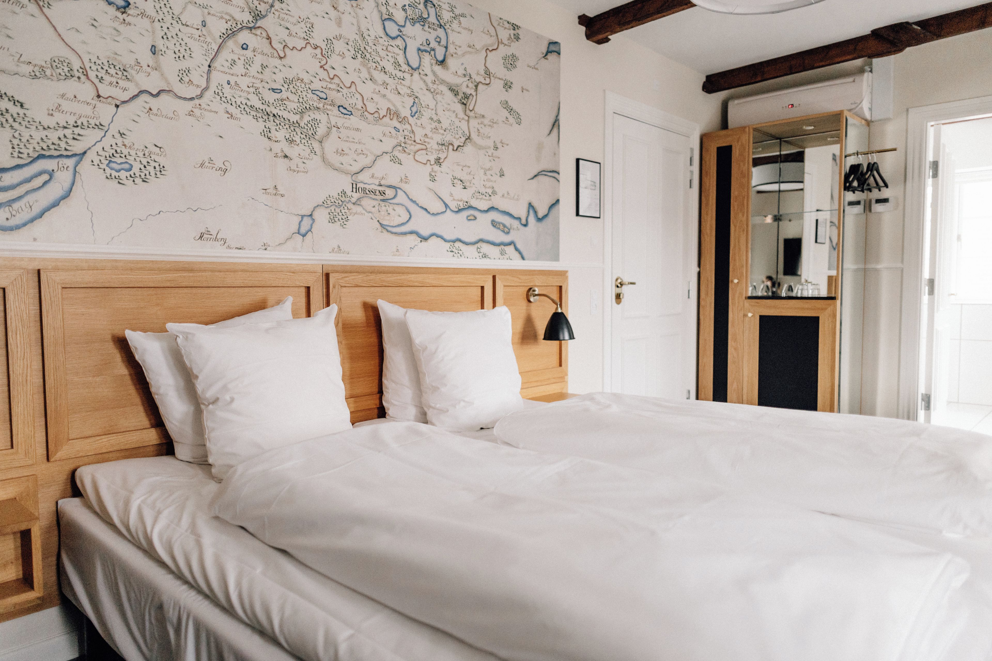 A bed with white bedding and a wooden headboard, a map on the wall, and a mirror with a wooden frame.