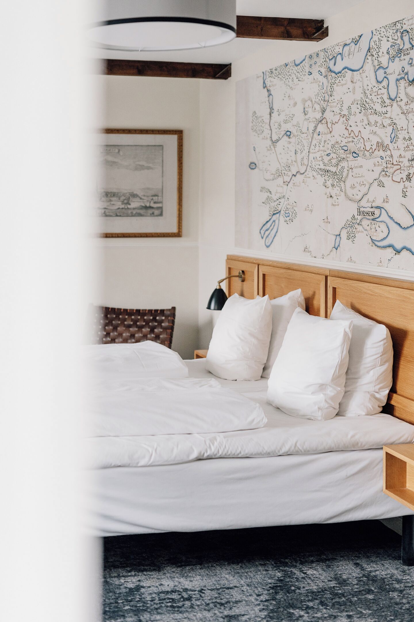 A neatly made bed with white linens and pillows, a wooden headboard, a map on the wall, and a framed picture above the bed.