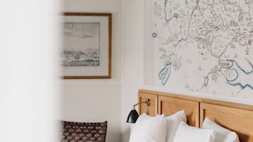 A neatly made bed with white linens and pillows, a wooden headboard, a map on the wall, and a framed picture above the bed.