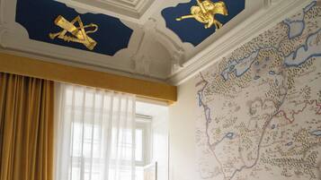 A room with a bed, a window with curtains, and a map on the wall.