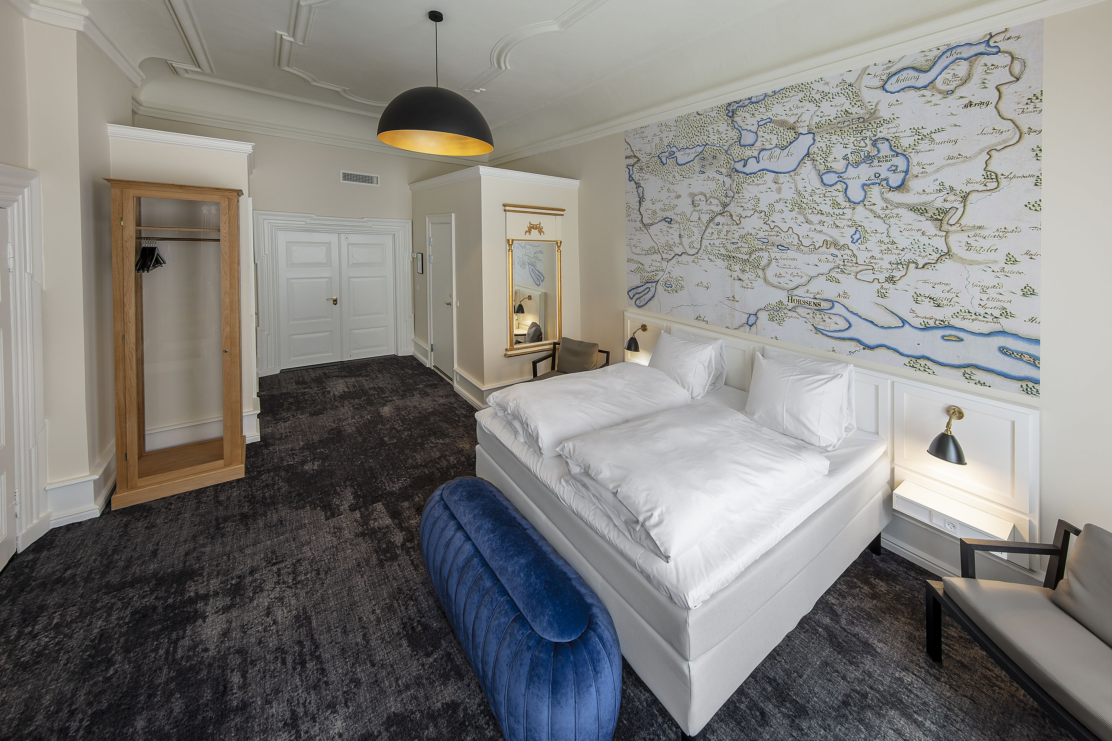 A bedroom with a large map on the wall, a bed, a wardrobe, and a bench.