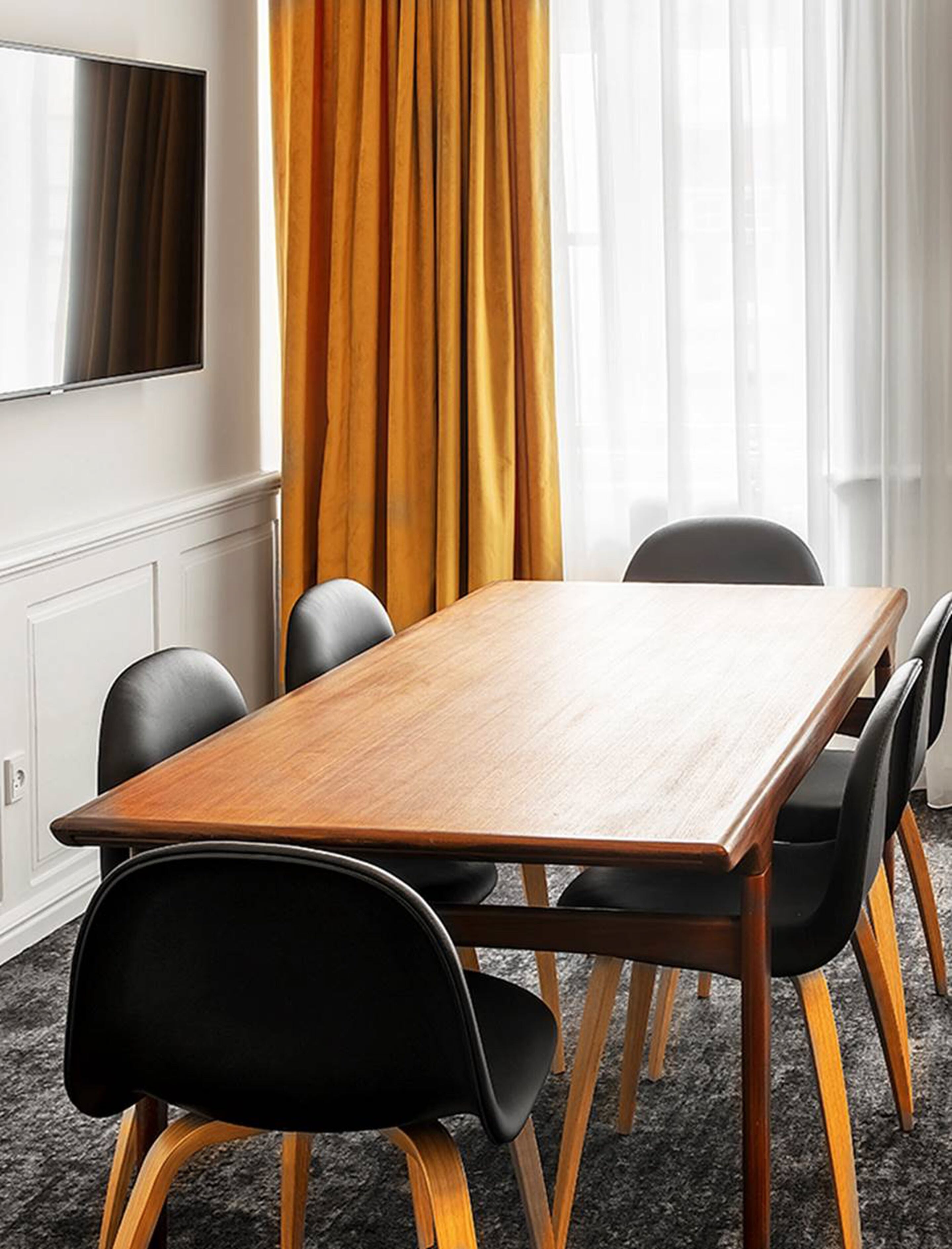 A conference room with a wooden table, black chairs, and a large window with curtains.