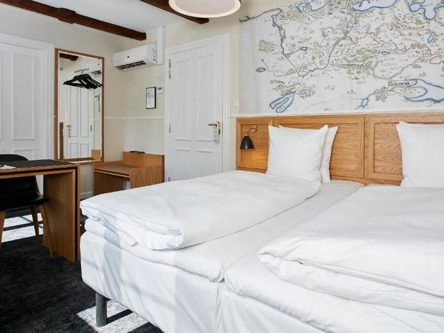 A hotel room with two beds, a desk, a chair, a map on the wall, and a mirror.
