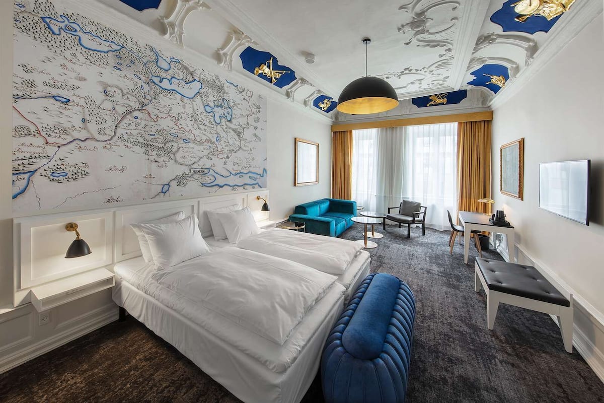 Une chambre d’hôtel avec une grande carte accrochée au mur, un lit, un canapé bleu, un bureau et un téléviseur.