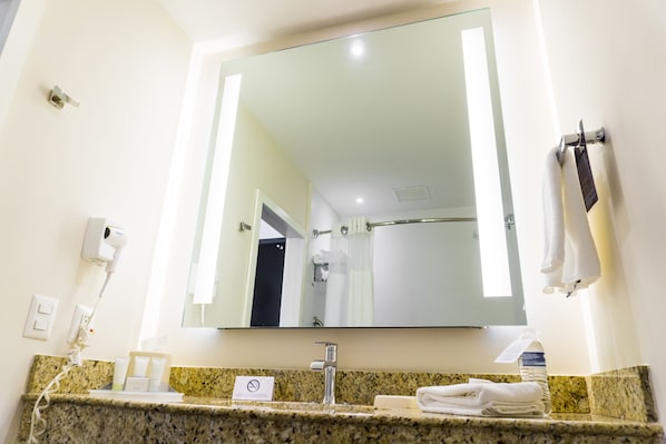 A hotel bathroom with a large mirror, granite countertop, towel rack, and a hairdryer on the wall. - Courtyard by Marriott San Luis Potosi (San Luis Potosi)