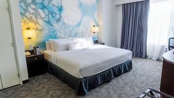 Una habitación de hotel con una cama grande, dos mesitas de noche con lámparas, un escritorio con una silla y una ventana con cortinas.